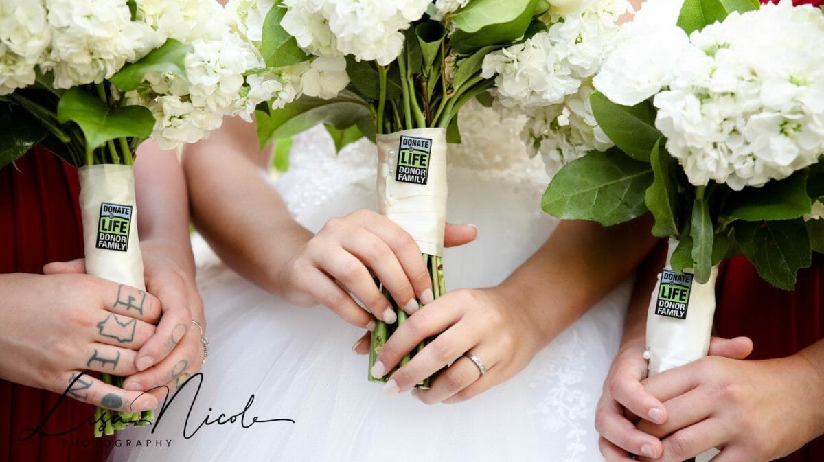 Three sets of hands holding three bouquets of flowers with Donate Life Donor Family logo on them.