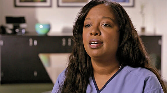A woman wearing blue scrubs talking to the camera