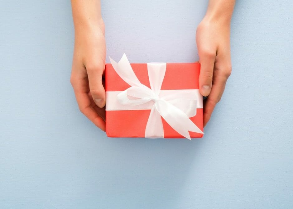 Manos femeninas sosteniendo caja de regalo roja con lazo blanco