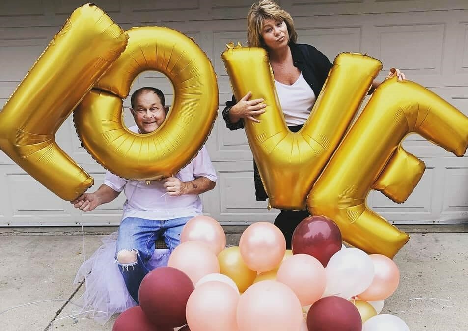 A man and a woman posing with gold balloon letters that spell Love