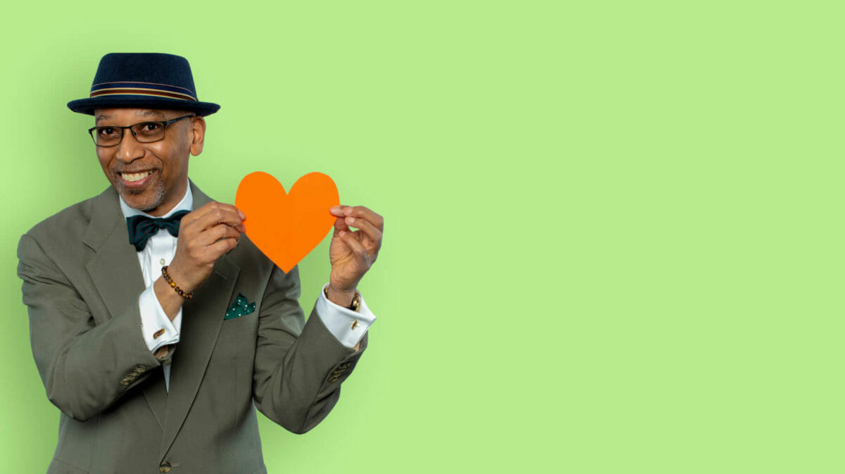 Man in suit with bow tie and hat, holding a cutout paper heart