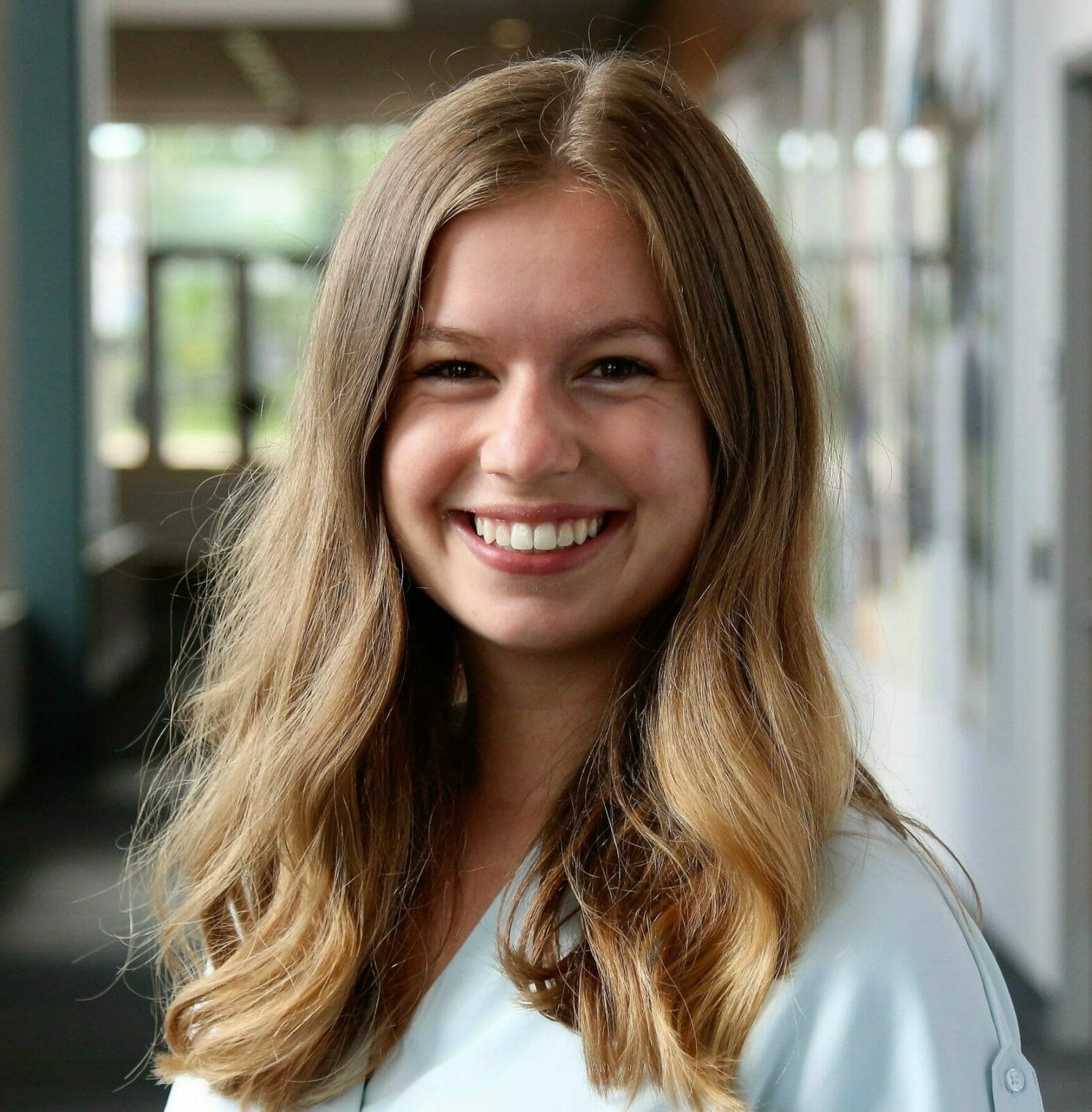 Woman in blue collared shirt smiles into the camera.