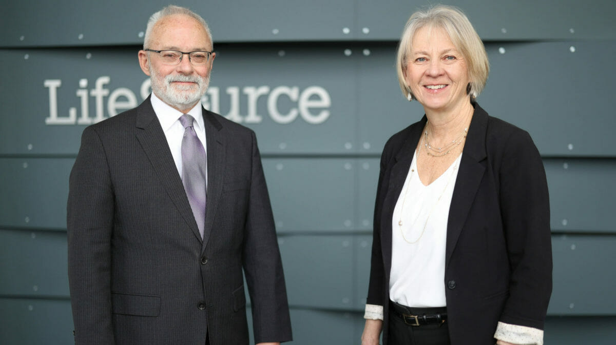 man and woman in business attire stand smiling at camera