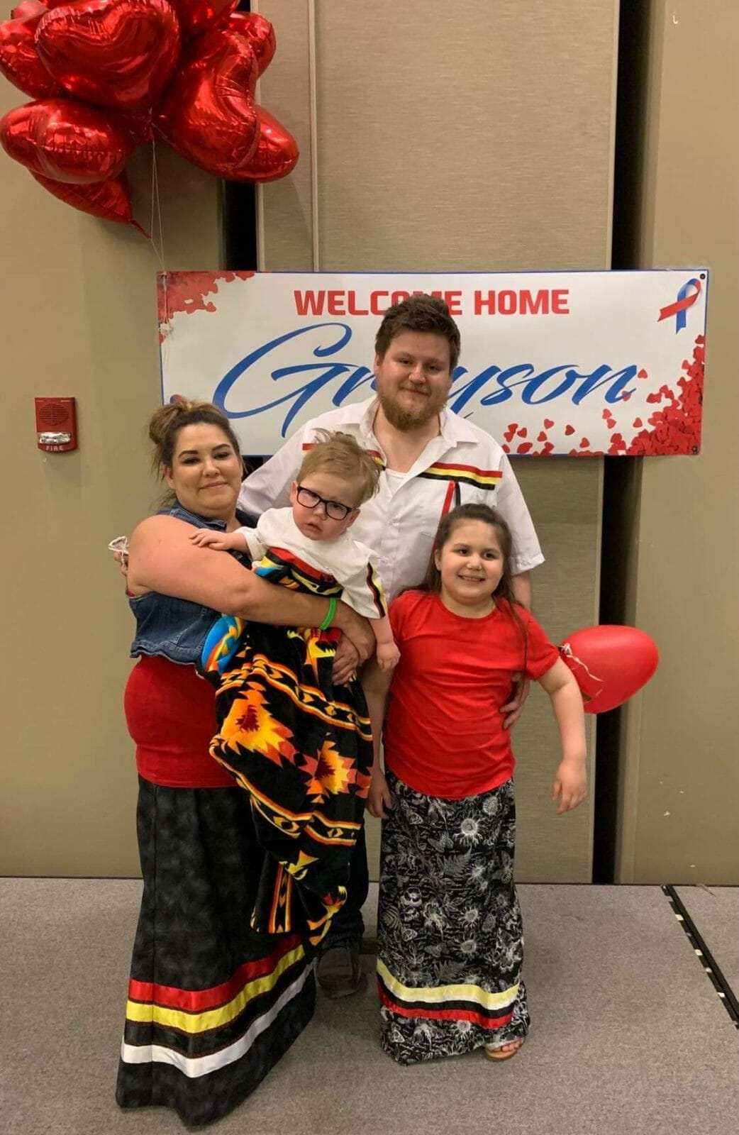 Mom, Dad, Daughter and Baby in front of Welcome Home Greyson sign