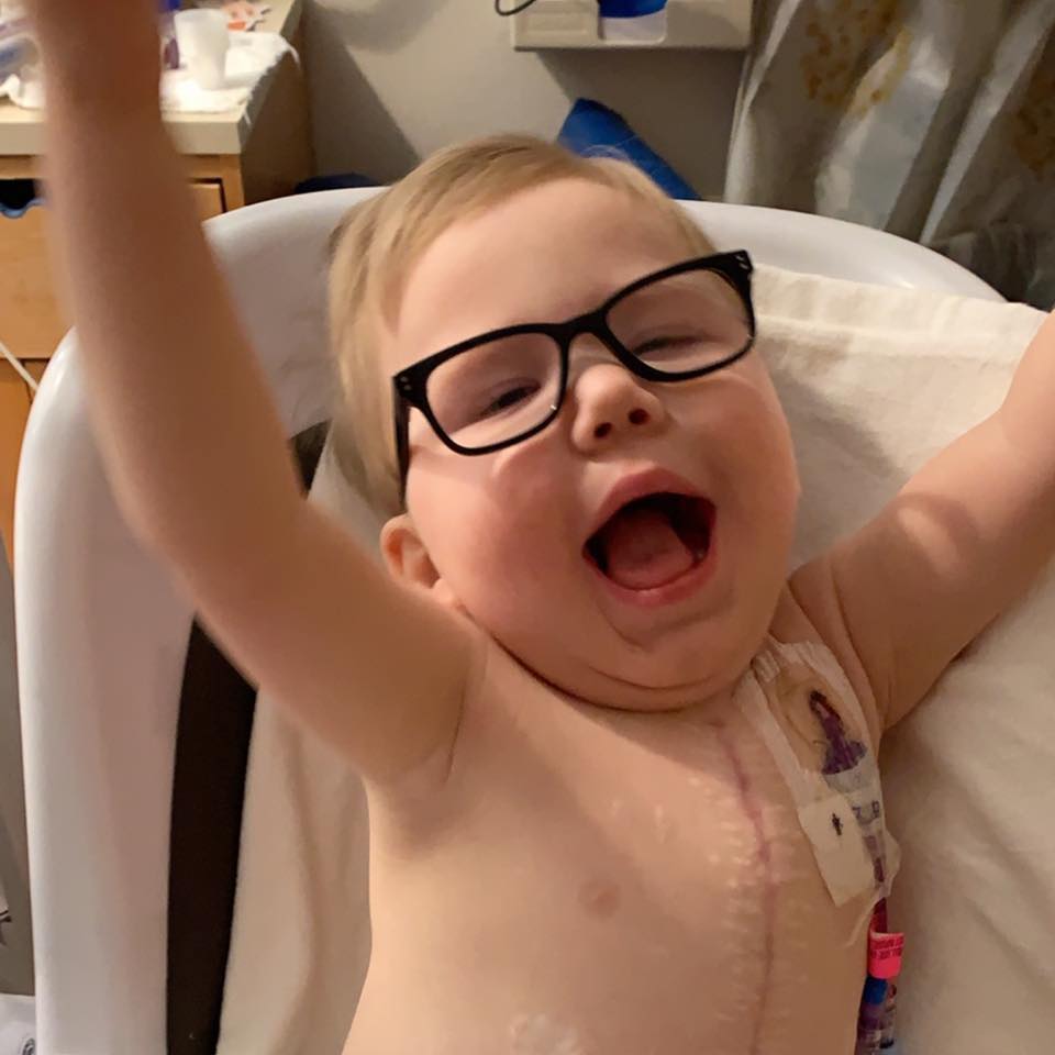 little boy with glasses raises arms in air with joy