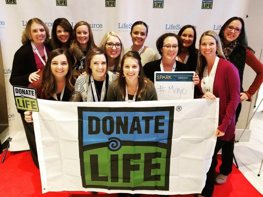 Women holding a DonateLife flag smile at the camera with a #Mayo sign.