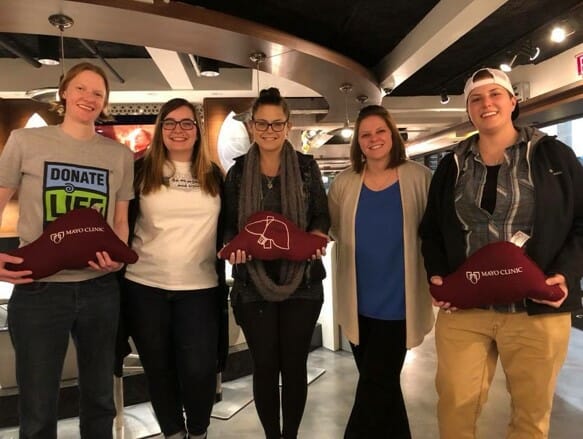 Five women holding plush livers smile at camera