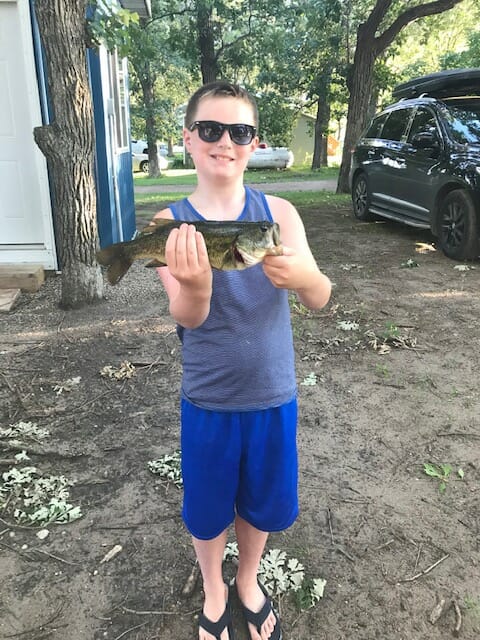 Caleb, wearing sunglasses smiles at camera while holding catch of the day.