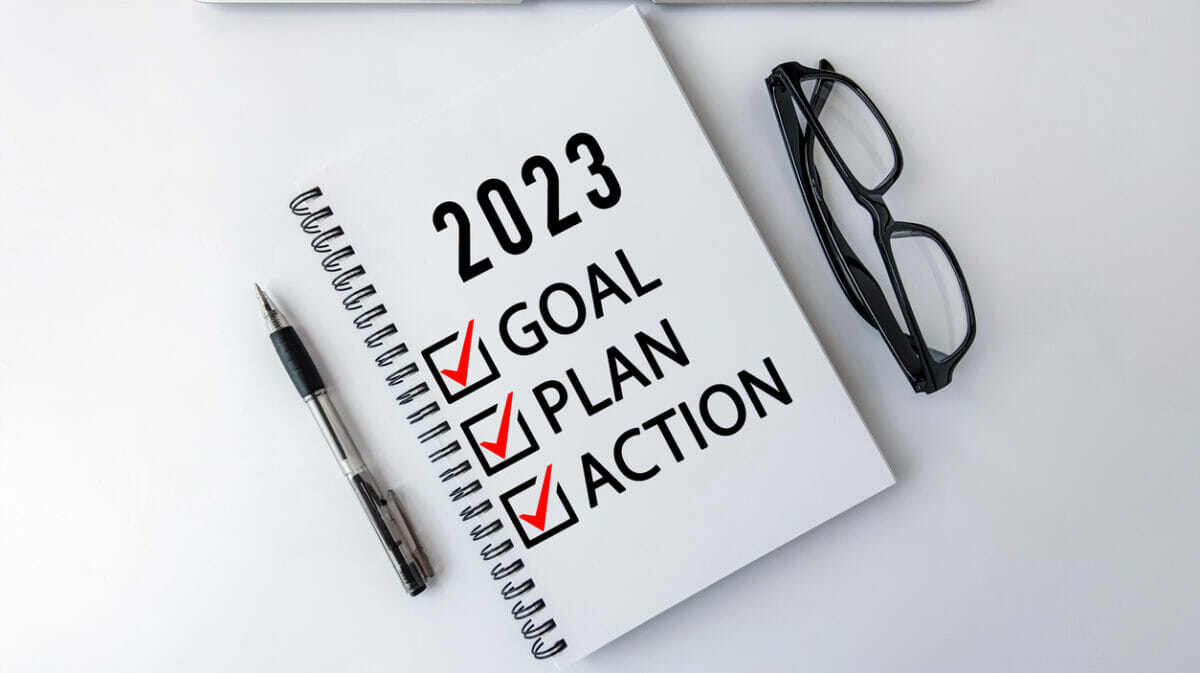 2023 Goal, Plan, Action checklist text on note pad with laptop, glasses and pen.