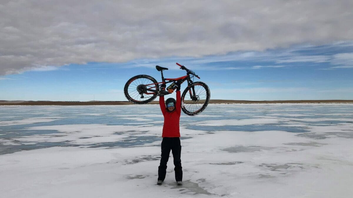 woman holds bike over head in triumph on icy landscape