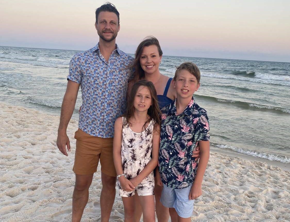 Mamá, papá, hijo e hija sonríen a la cámara frente a una puesta de sol en el océano