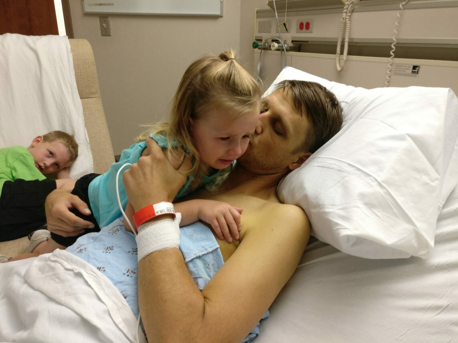 Padre en cama de hospital consuela a niños llorosos y preocupados.