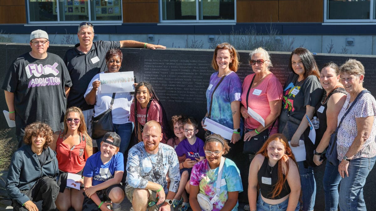 Multiple generations of a family stand and kneel in front of the memorial wall in the LifeSource Donor Garden.