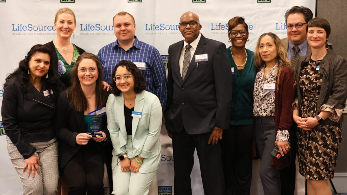 People in front of photo background smiling at the camera with their award.